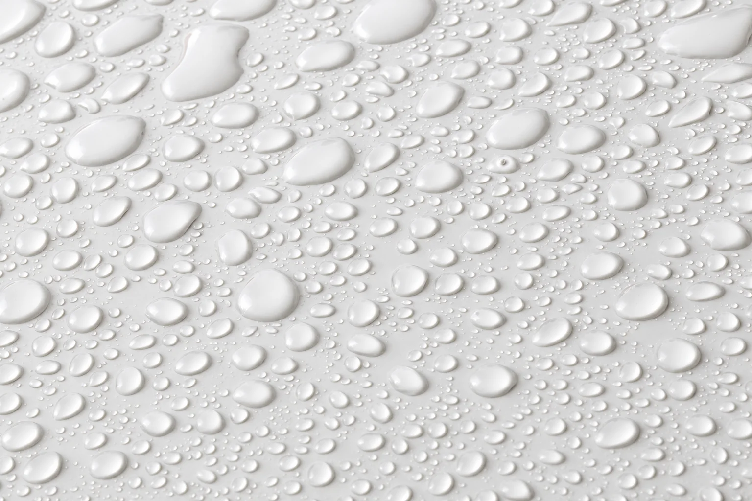 Gros plan de nombreuses gouttes d'eau de différentes tailles perlant sur une surface lisse de couleur blanche.