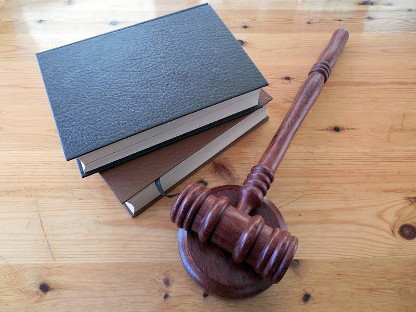 Un maillet de juge en bois foncé et son socle sont posés sur une table en bois clair, à côté de deux livres reliés de cuir.
